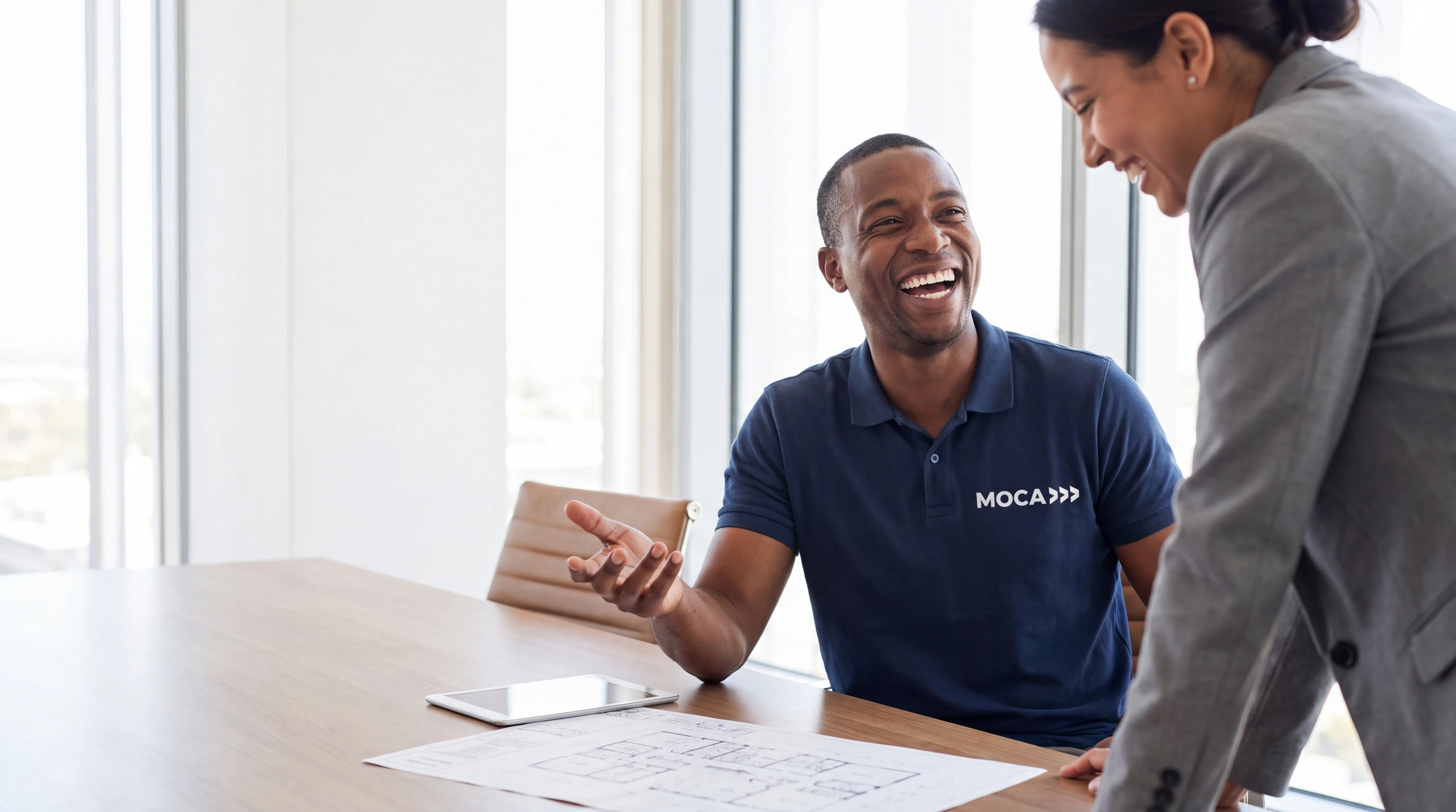A MOCA project manager laughing with a customer over a plan on the table