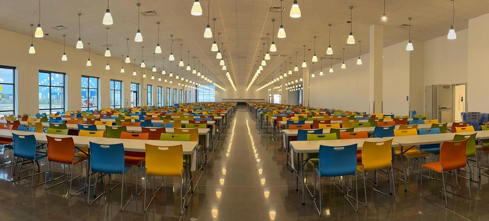 A finished associate breakroom fitted out by MOCA: long rows of tables and colourful chairs under pendant lights